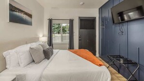 Un dormitorio con una cama, un televisor montado en la pared, una ventana con cortinas y una puerta.