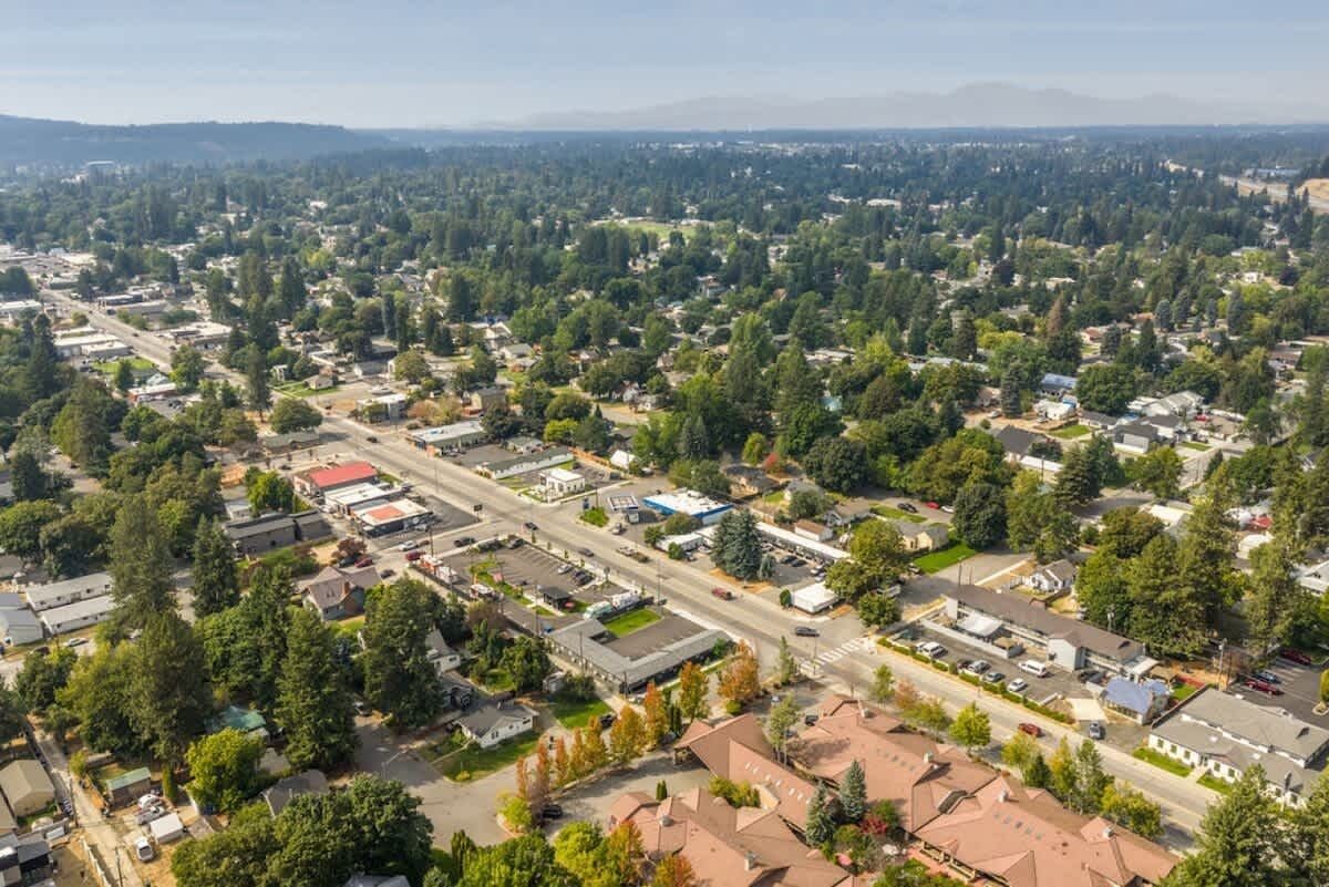 An aerial view of a suburban area with residential houses, commercial buildings, and a main road.