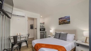 Une chambre d’hôtel équipée d’un lit, d’un bureau, d’une chaise, d’une télévision, d’un climatiseur, d’un four à micro-ondes et d’un tableau au mur.