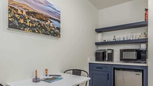 A compact kitchen with a white table, two black chairs, a microwave, a dishwasher, and a shelf with kitchenware. - Studio #3 At The Flats - Downtown Nightlife (Coeur d'Alene)