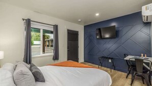 A modern hotel room with a large bed, a desk, and a TV mounted on the wall.