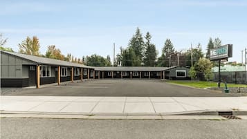 Un motel con una fila de habitaciones, un área de estacionamiento techada y un letrero que dice 'The Flats'.