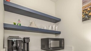 A compact kitchen with a stainless steel refrigerator, a microwave, a coffee maker, and a dishwasher. There are blue cabinets and a white countertop.