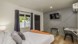 Ein modernes Hotelzimmer mit Bett, Schreibtisch, Stuhl, Wandfernseher und einem Fenster mit Vorhängen.