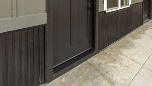 Eine dunkel gefärbte Haustür mit einem kleinen Fenster darüber, ein weiß gefasstes Fenster zur Rechten und die Zahl '11' an der Wand.