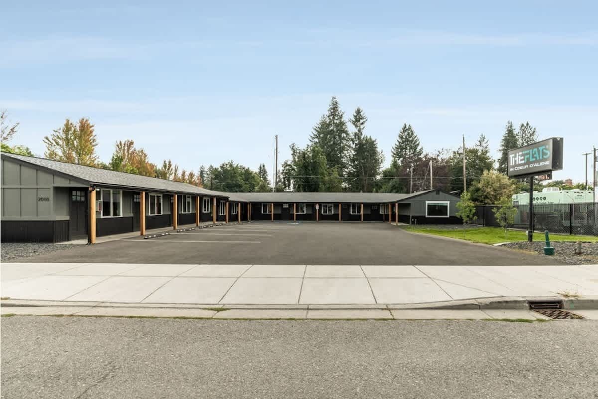 Un motel con una fila de habitaciones, un área de estacionamiento techada y un letrero que dice 'The Flats'.