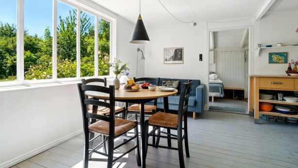 A bright dining area with a round table and chairs, a blue sofa, and a view of greenery through large windows. - "Krister" - 900m from the sea by Interhome (Hasle)