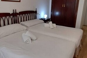 Ein ordentlich bezogenes Bett mit weißen Leinen und Kissen, ein Nachttisch mit Lampe und eine Holztür im Hintergrund.
