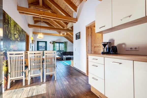 A modern kitchen with wooden beams, a dining area with chairs, and a living room with a sofa.