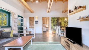 A cozy living room with a sofa, a coffee table, a TV, wooden shelves, and a bookshelf. - Apartment 'Blockhaus - Ferienwohnung Sunset' with Shared Garden (Augustusburg-Erdmannsdorf)