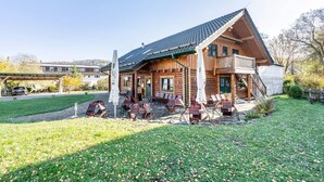 A wooden lodge with a covered patio, outdoor seating, and a staircase leading to the entrance. - Apartment 'Blockhaus - Ferienwohnung Sunset' with Shared Garden (Augustusburg-Erdmannsdorf)