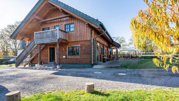 A wooden cabin with a balcony, a staircase, and a gravel driveway. - Apartment 'Blockhaus - Ferienwohnung Sunset' with Shared Garden (Augustusburg-Erdmannsdorf)