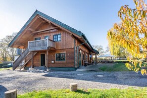 A wooden cabin with a balcony, a staircase, and a gravel driveway. - Apartment 'Blockhaus - Ferienwohnung Sunset' with Shared Garden (Augustusburg-Erdmannsdorf)
