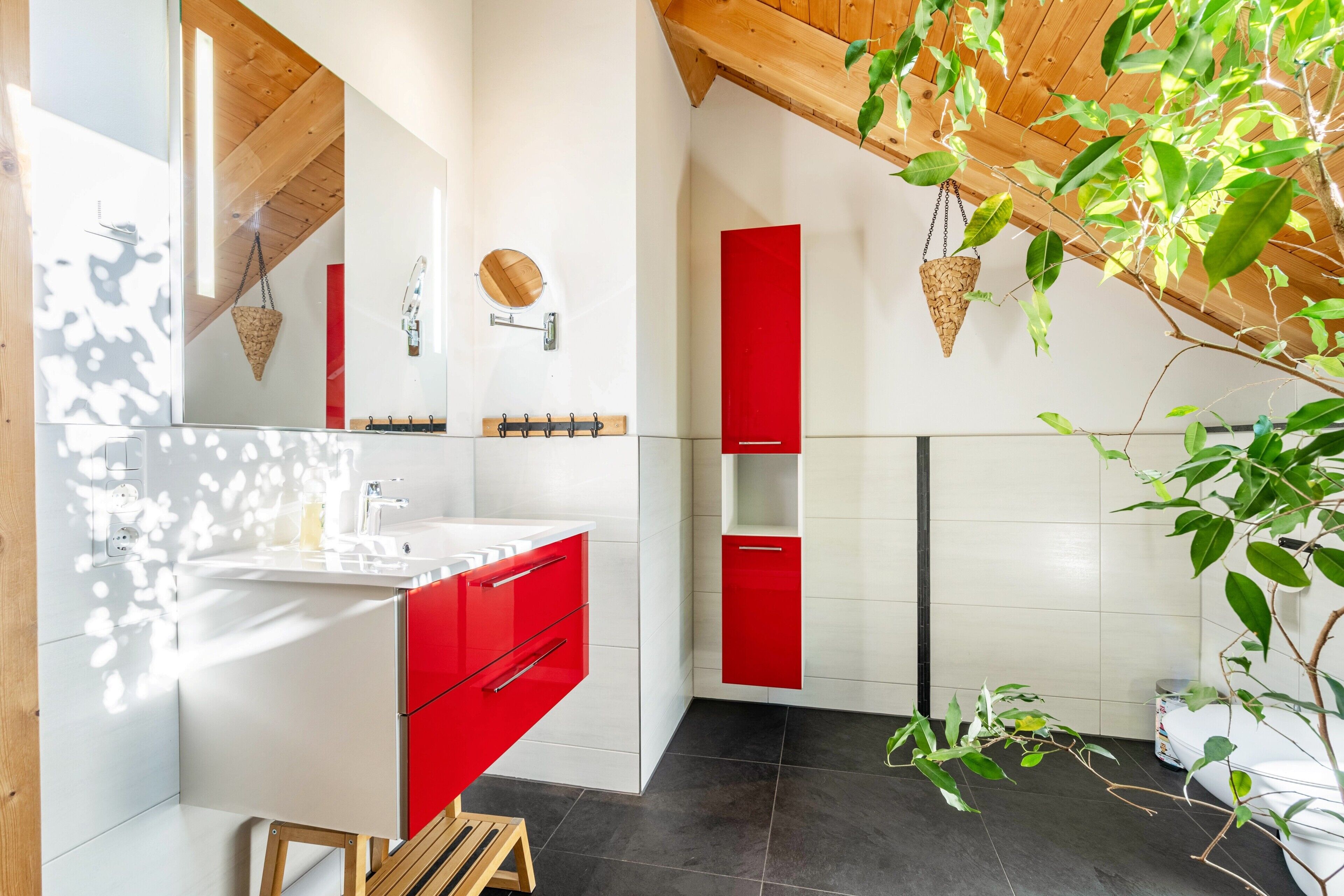 A modern bathroom with a white sink, red cabinets, and a wooden ceiling.