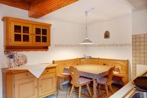 A kitchen with wooden cabinets, a dining table with chairs, a hanging light fixture, and a tiled backsplash. - Apartment 'Zum Schnitzer Franzl' with Mountain View and Wi-Fi (Garmisch-Partenkirchen)
