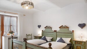 A bedroom with a double bed, two bedside tables, a nightstand, a window with curtains, and a chandelier.