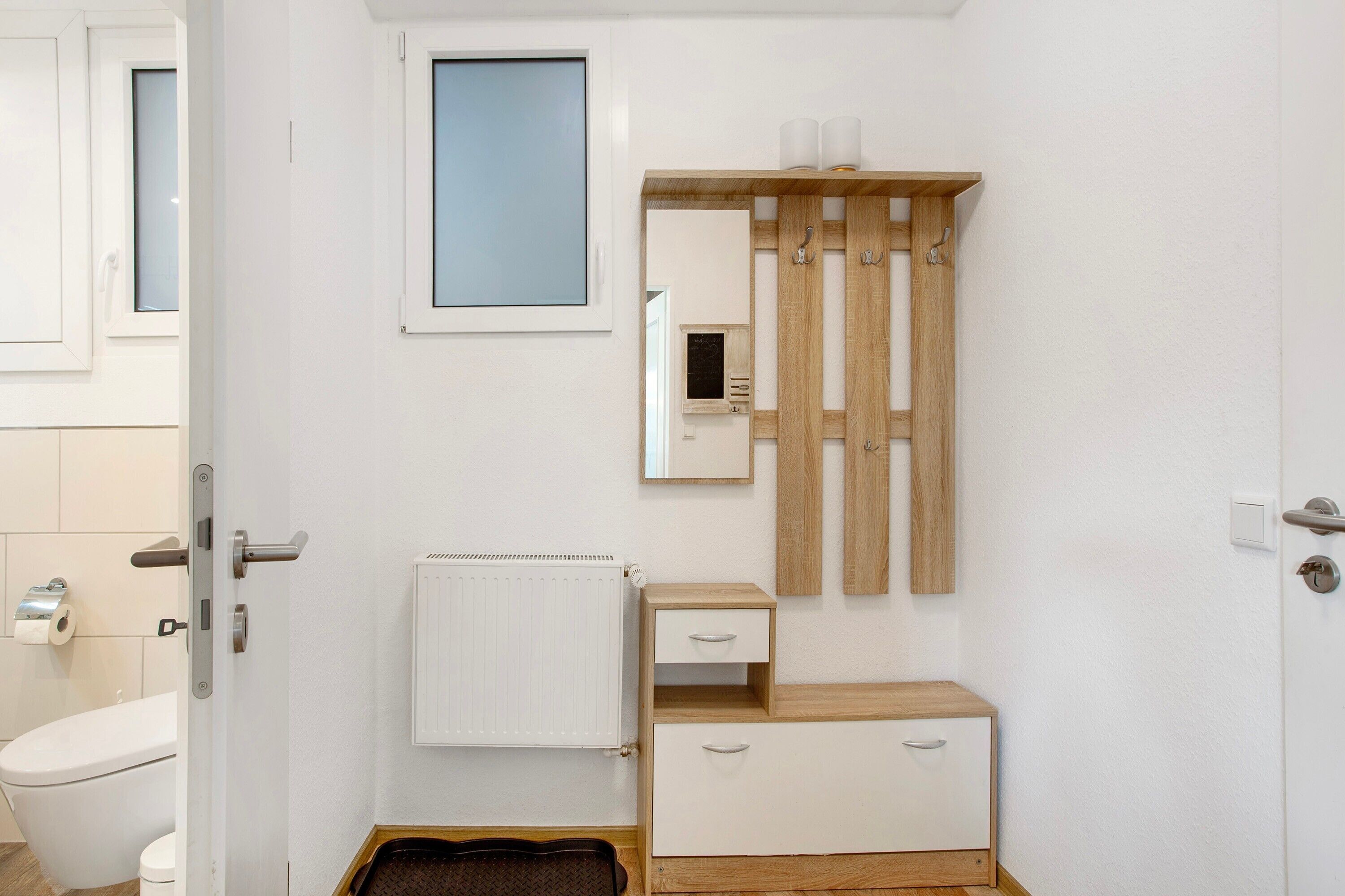 A bathroom with a toilet, a radiator, a wooden cabinet, a mirror, and a window.