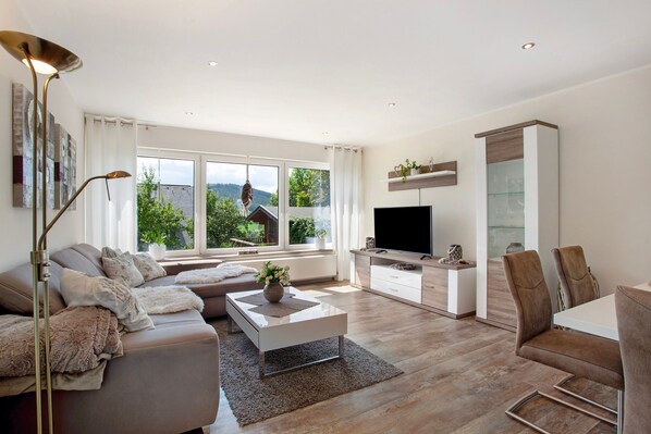 A modern living room with a sofa, coffee table, TV, and dining area.