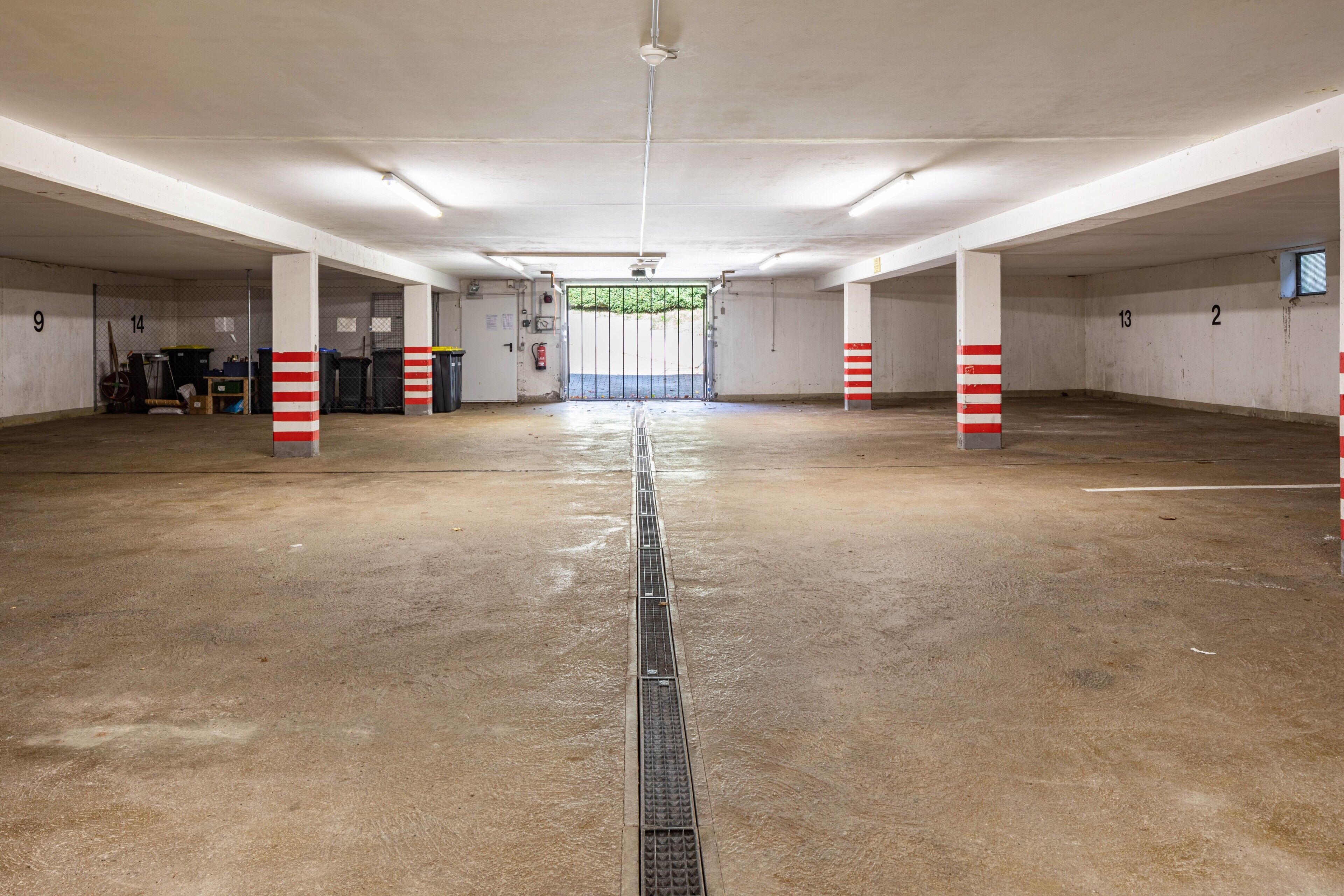 Un grand parking intérieur, doté de planchers en béton, de murs blancs et de piliers à rayures rouges.