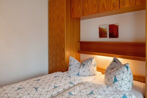Quarto com cabeceira de madeira, roupa de cama com padrão geométrico e duas imagens penduradas na parede.