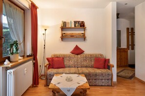 Un salon avec un canapé, une table recouverte d’une nappe, une bibliothèque et un radiateur.