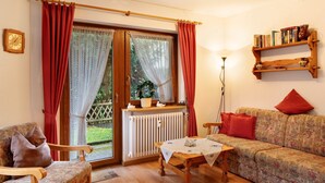 A cozy living room with a wooden floor, a sofa, a chair, a table with a white tablecloth, a radiator, and a bookshelf with books. - Apartment 'Nr 2' with Private Terrace, Private Garden and Wi-Fi (Titisee-Neustadt)