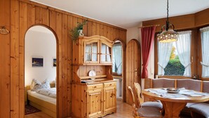 A wooden interior with a bed, a wooden cabinet, a dining table with chairs, and a window with curtains. - Apartment 'Nr 2' with Private Terrace, Private Garden and Wi-Fi (Titisee-Neustadt)