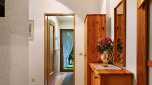 A hallway with a wooden cabinet, a vase with flowers, and a door leading to a room with a view of greenery. - Apartment 'Nr 2' with Private Terrace, Private Garden and Wi-Fi (Titisee-Neustadt)