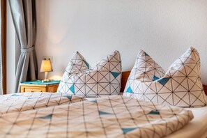 Een bed met geometrische kussens, een bedlampje en een houten nachtkastje.