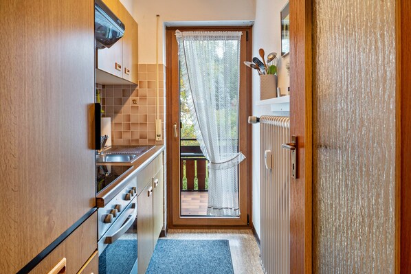 Eine schmale Küche mit Holzausbau, einem Herd und einem Fenster mit Vorhang.
