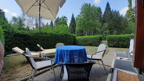 Un patio con un tavolo ricoperto da una tovaglia blu, due poltrone e un ombrellone grande.