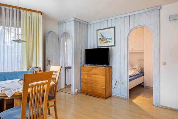 Quarto com uma mesa de jantar, cadeiras, televisão em um armário de madeira, cama com travesseiros e um quadro na parede.