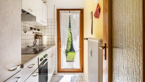 Una cucina con mobili bianchi, un piano di lavoro e una porta che dà su un giardino.