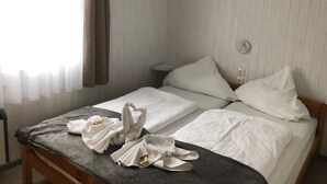 Een net opgemaakt bed met witte lakens, een grijze deken en een handdoek gevouwen in de vorm van een zwaan.