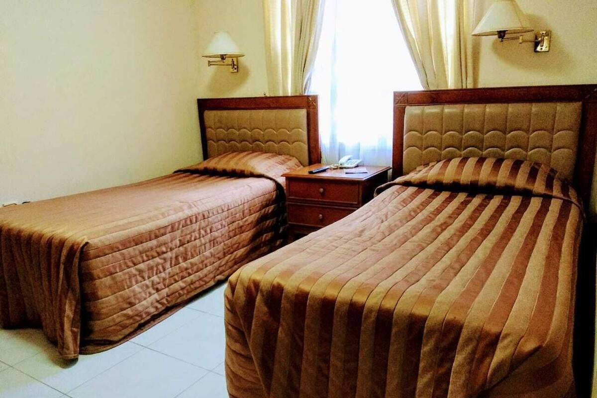 A hotel room with two beds, a nightstand, and a lamp.