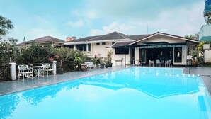 A swimming pool with a patio area, outdoor seating, and a building with a tiled roof.