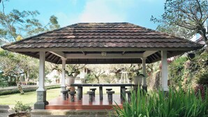 A gazebo with a tiled roof, surrounded by greenery and a paved area with benches.