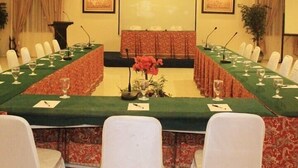 A conference room with a long table, white chairs, microphones, and floral centerpieces.
