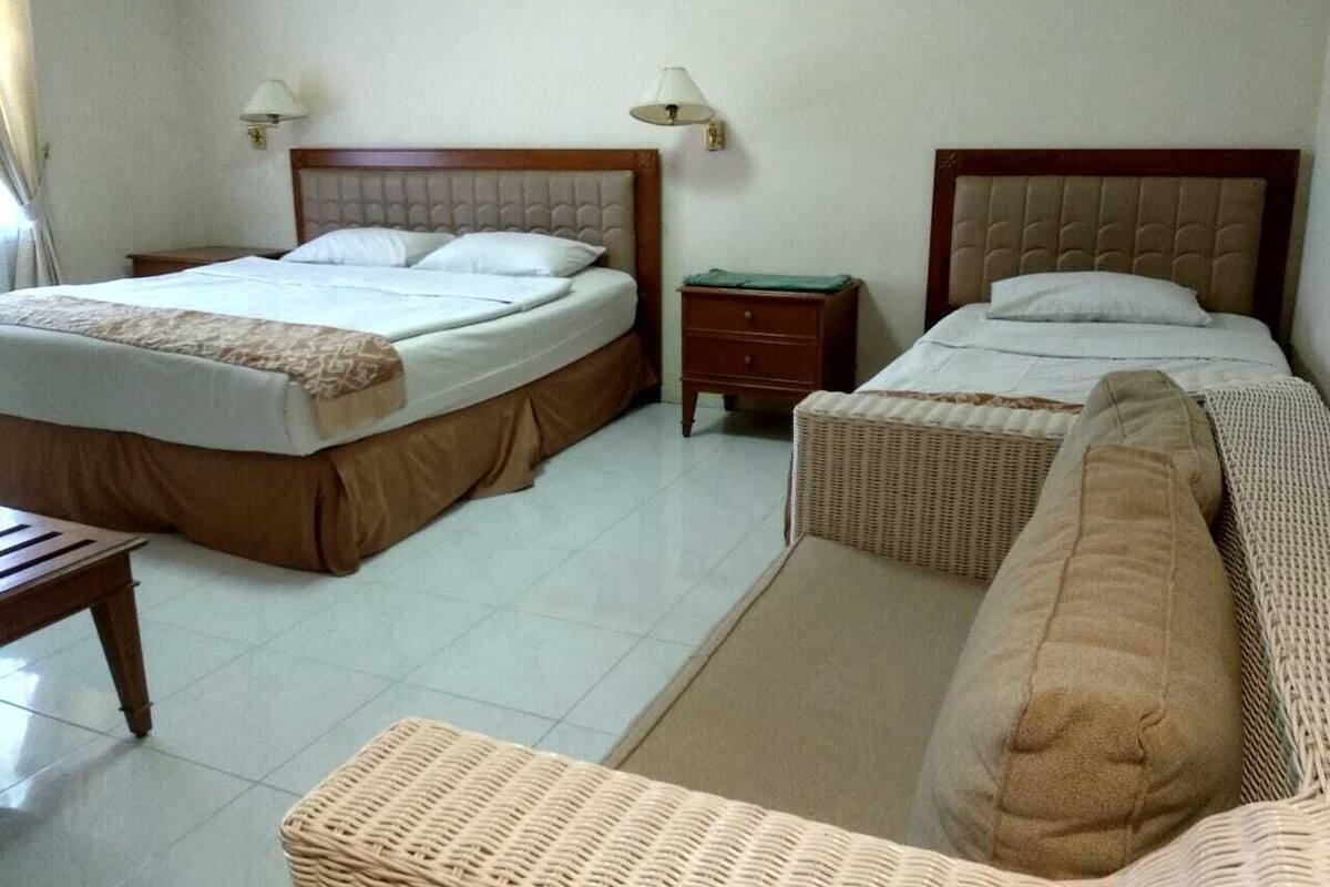 A hotel room with two beds, a small table, a nightstand, and a wicker chair.