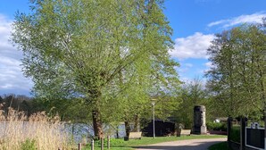 A paved pathway leading to a statue, surrounded by trees and a body of water.