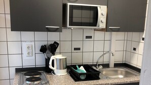 A compact kitchen with a microwave, stove, sink, and black cabinets.