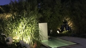 Un espace piscine extérieure, utilisable la nuit, protégé par une enceinte en verre et entouré d’une végétation luxuriante, le sol étant recouvert de neige.
