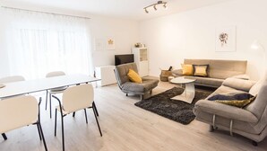 Un salon moderne comprenant une table à manger, des chaises, un canapé, un téléviseur et un meuble.