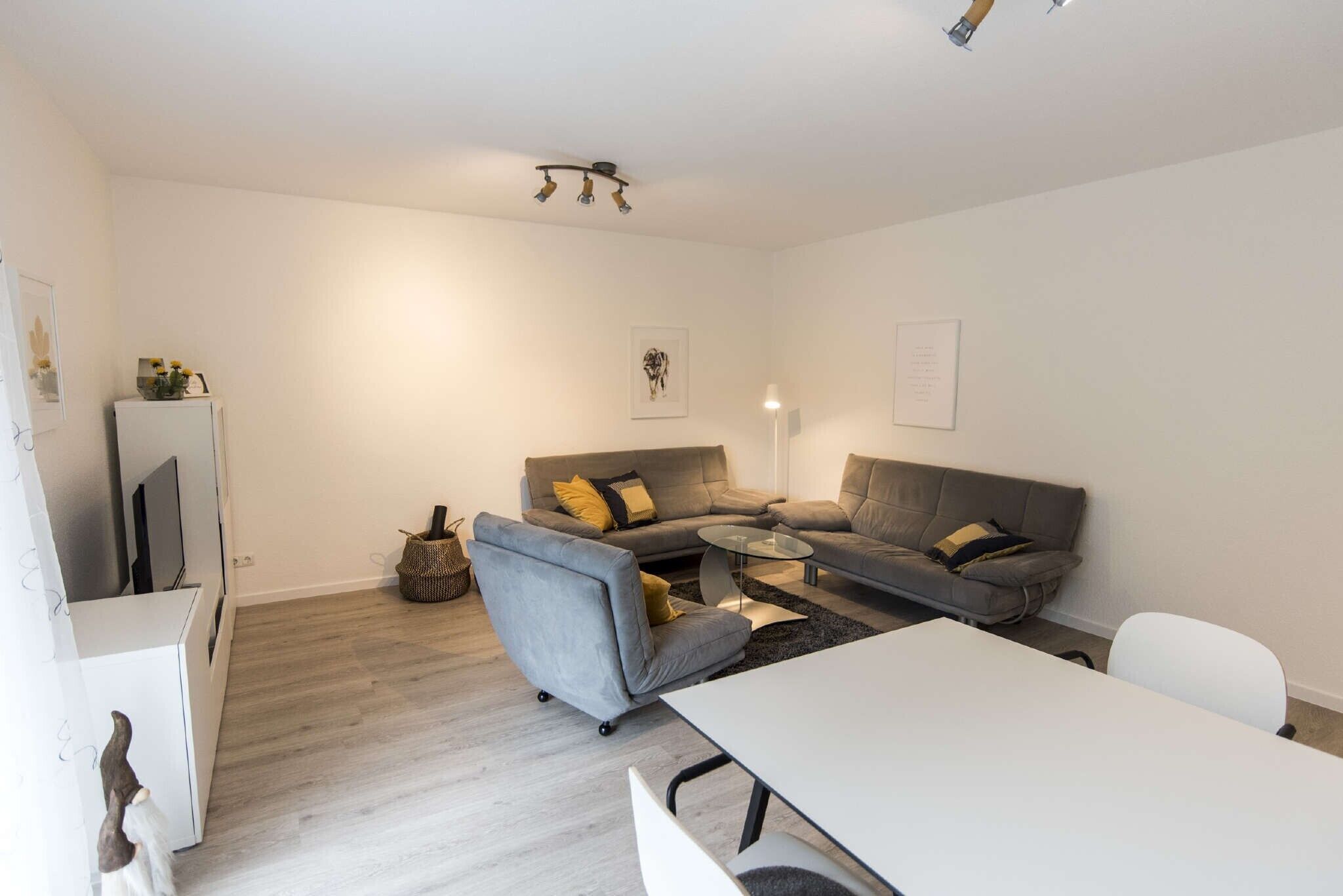 A modern living room with a grey sofa, a white coffee table, and a white TV stand.