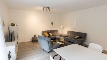 A modern living room with a grey sofa, a white coffee table, and a white TV stand.