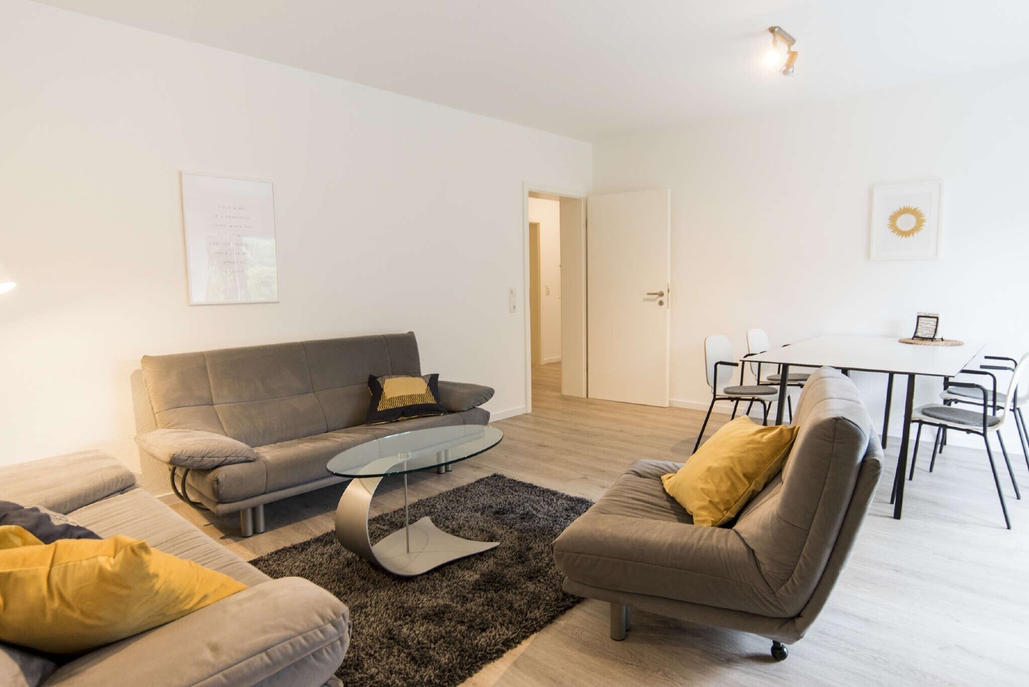 Ein modernes Wohnzimmer mit einer Couch, Sesseln, einem Glastisch und einem Essbereich mit Tisch und Stühlen.