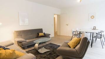 Ein modernes Wohnzimmer mit einer Couch, Sesseln, einem Glastisch und einem Essbereich mit Tisch und Stühlen.