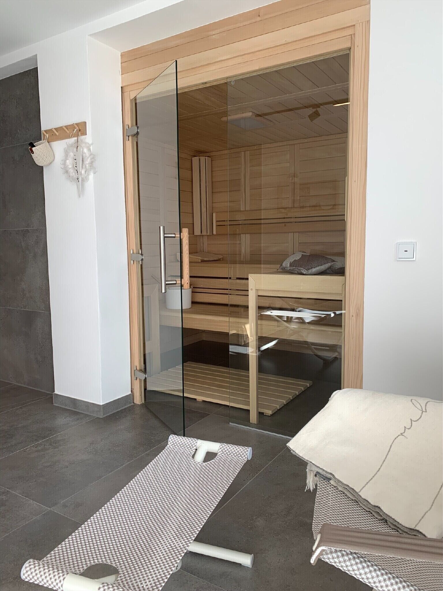 Une chambre moderne dotée d’une porte en verre donnant sur un sauna, d’un banc en bois et d’une petite table avec un coussin.