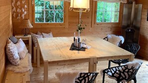 Un intérieur en bois comprenant une table à manger, des chaises, un luminaire suspendu et des fenêtres donnant sur un espace verdoyant.