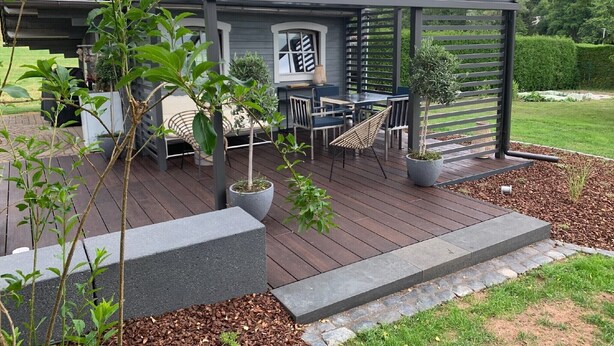 Une terrasse extérieure couverte, aménagée avec un espace repas, des sièges et des plantes en pot.